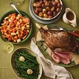 Roast lamb dinner with roasted root vegetables, baby potatoes, green beans, and gravy on a family meal table.